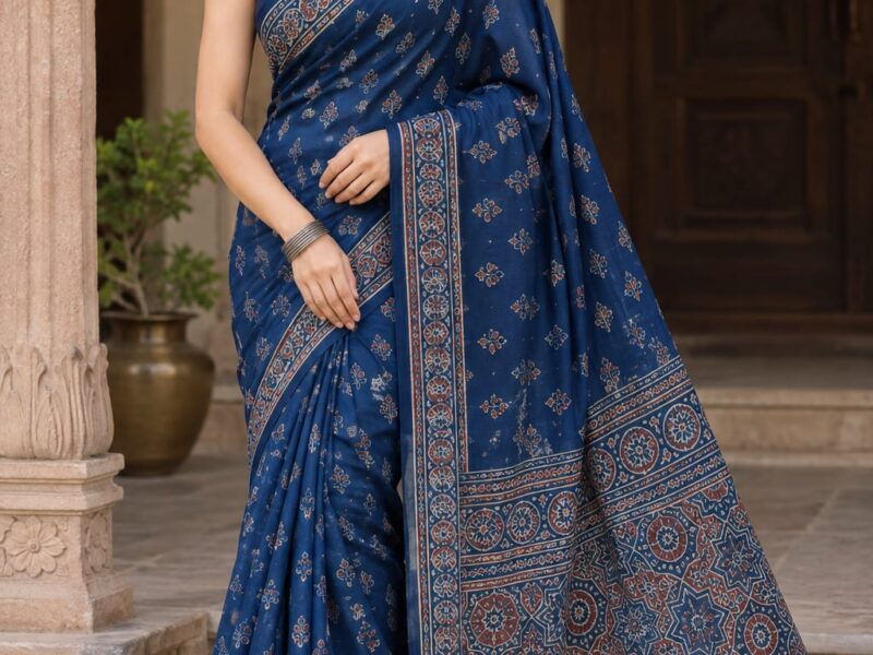 wearing a deep blue block-printed cotton saree with copper motifs, a matching sleeveless blouse, and traditional silver earrings.